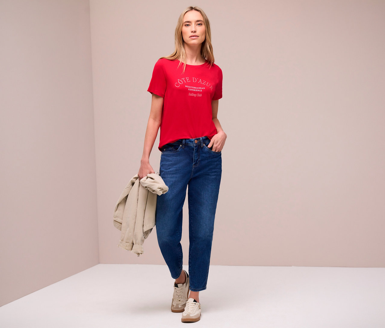 Frau in Jeans und rotem Street One T-Shirt mit Aufdruck, hält eine Jacke in der Hand.