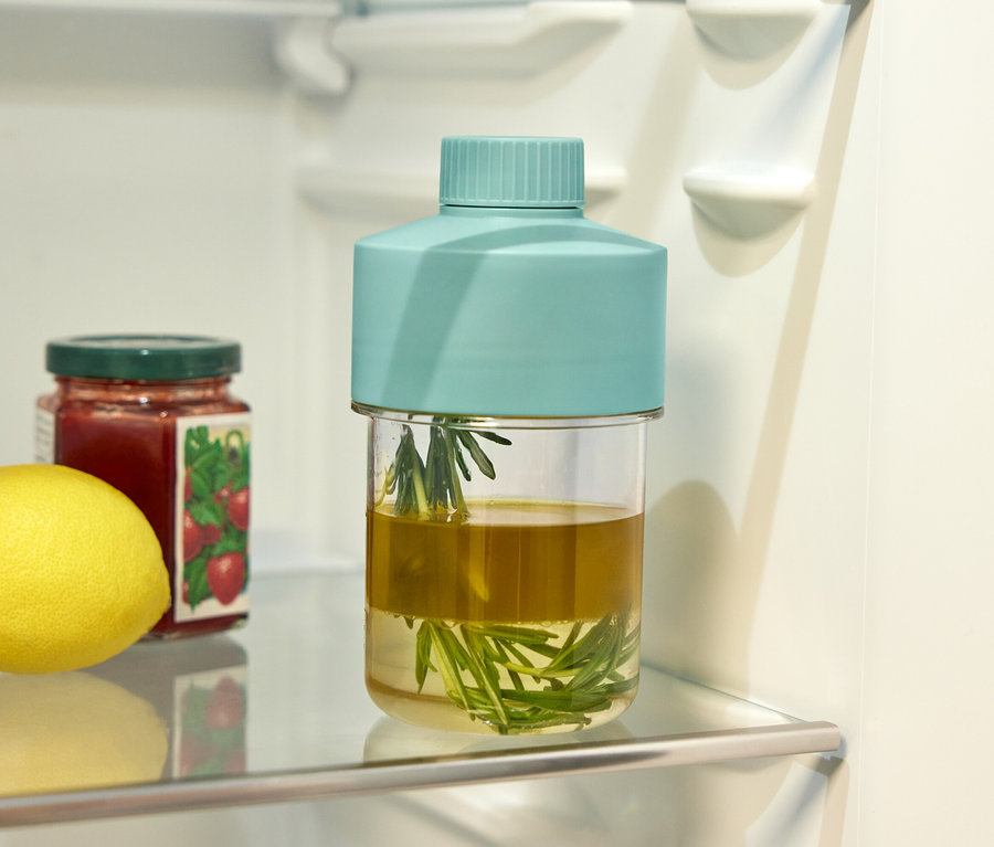 Auf einem Glasregal im Kühlschrank stehen eine Zitrone, ein Glas Erdbeermarmelade und ein Glas mit Kräutern in Öl.