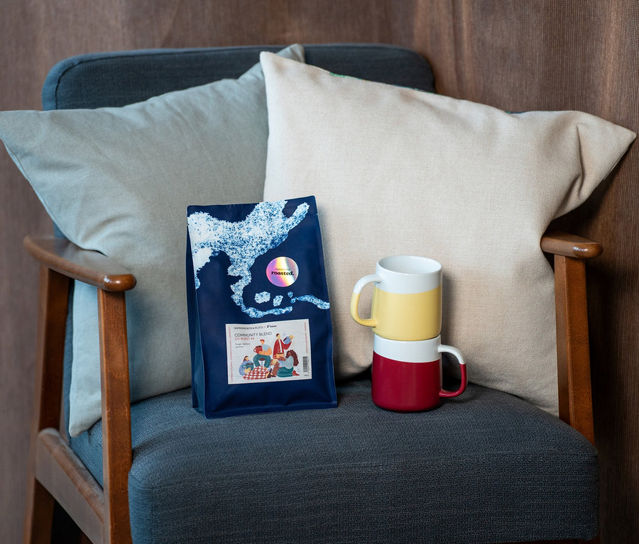 Auf einem Sessel liegen zwei Kissen, eine Kaffeepackung und zwei gestapelte Tassen.