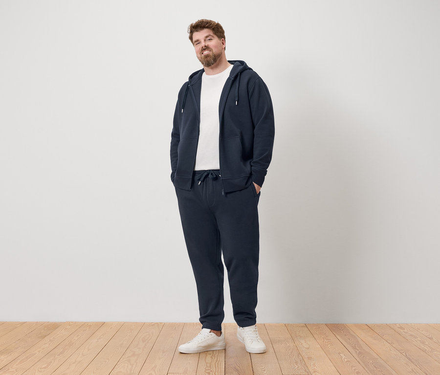 Mann steht in marineblauem Trainingsanzug und weißen Turnschuhen.