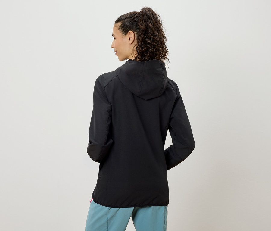 Rückansicht einer Frau mit Pferdeschwanz, die eine schwarze Kapuzenjacke und hellblaue Hosen trägt.