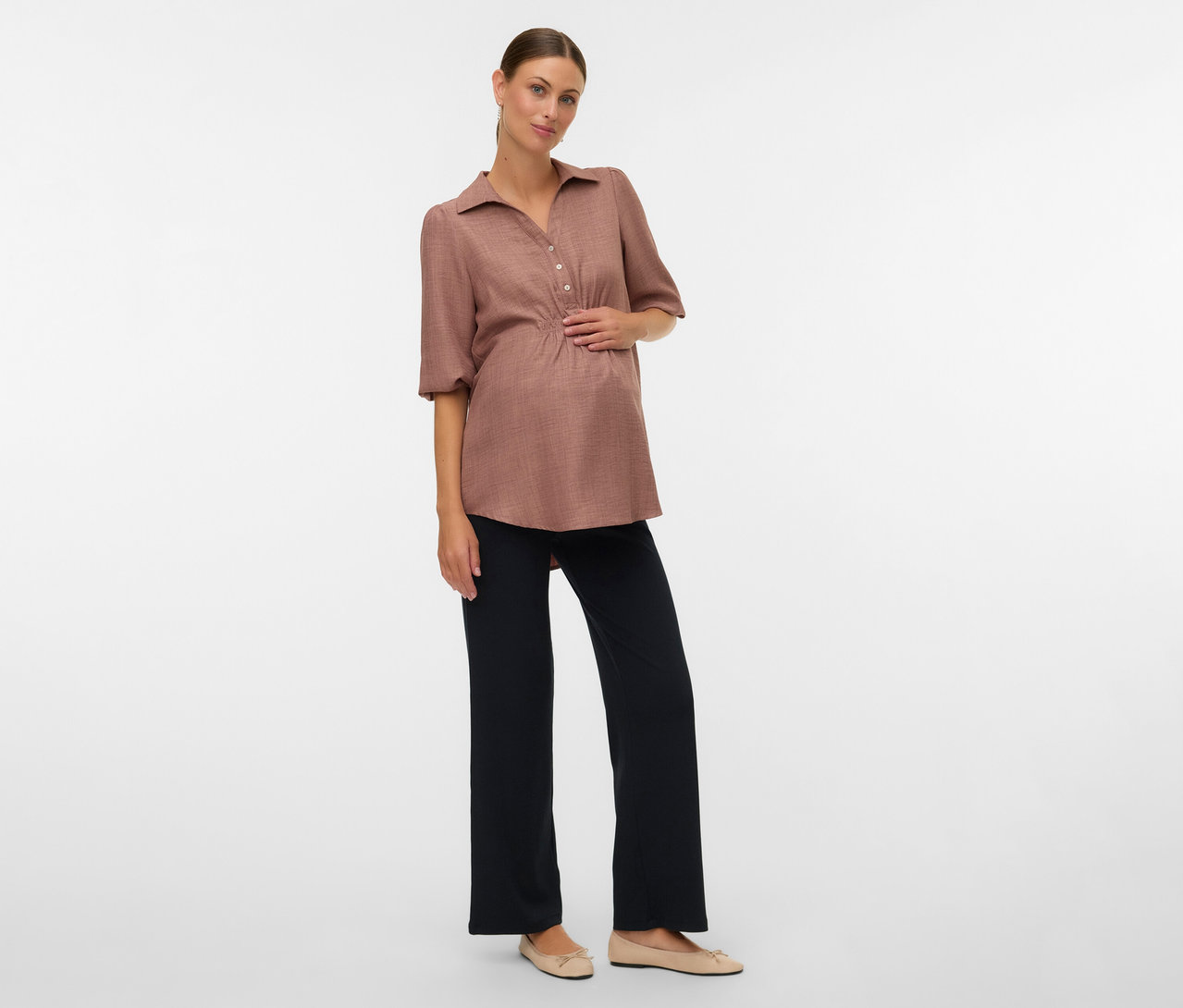 Schwangere Frau mit brauner Bluse und MAMALICIOUS lockeren Leggins »MLEMILY« posiert vor einem weißen Hintergrund.