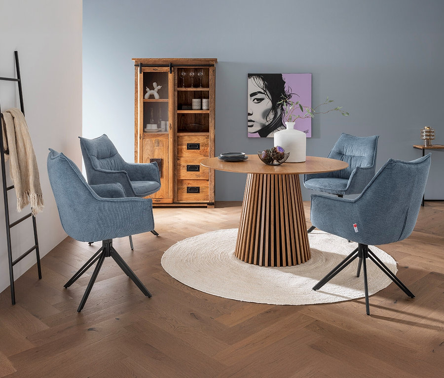 Ein Esstisch mit vier blauen, drehbaren DeVries »Ginosa« Diningsesseln umgeben von einem Teppich. Im Hintergrund befindet sich ein Holzschrank.