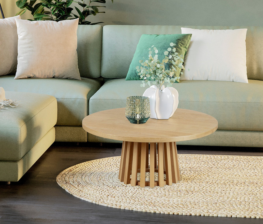 Ein grünes Sofa mit hellen Kissen und einem runden Tisch mit einer Vase und einem Windlicht darauf.