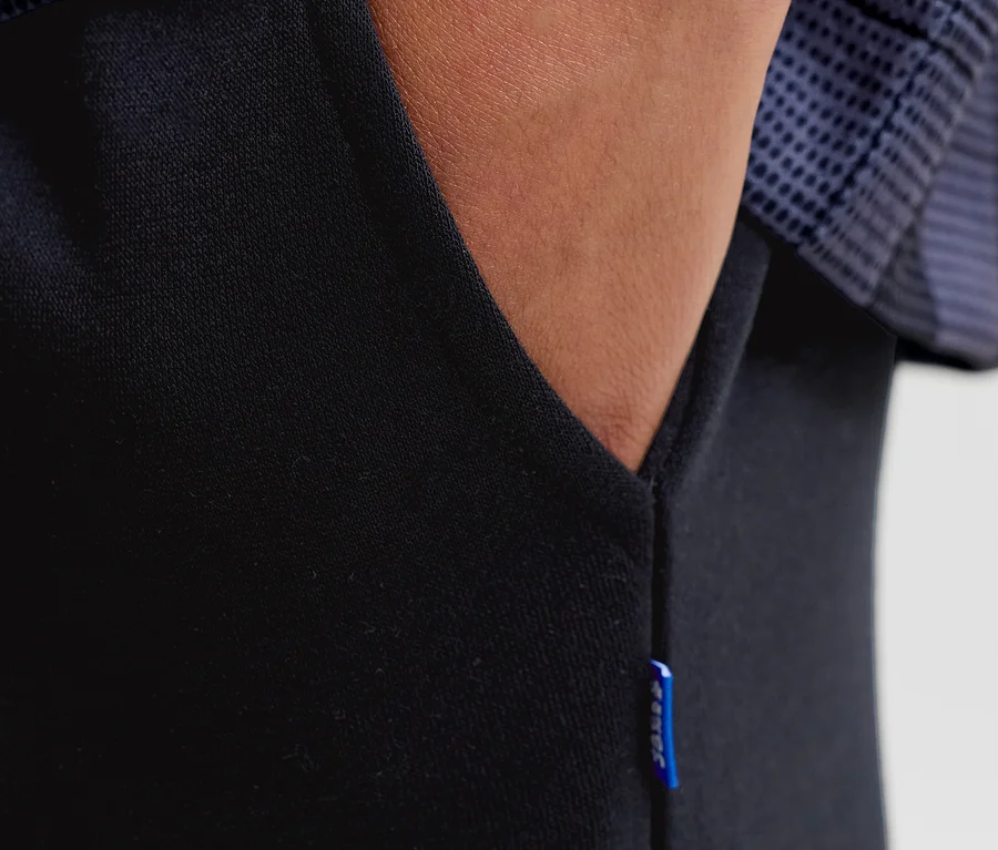 Nahaufnahme einer Hand in der Tasche einer schwarzen Jack&Jones Bradley Sweatpants, mit blauem Etikett an der Seite.