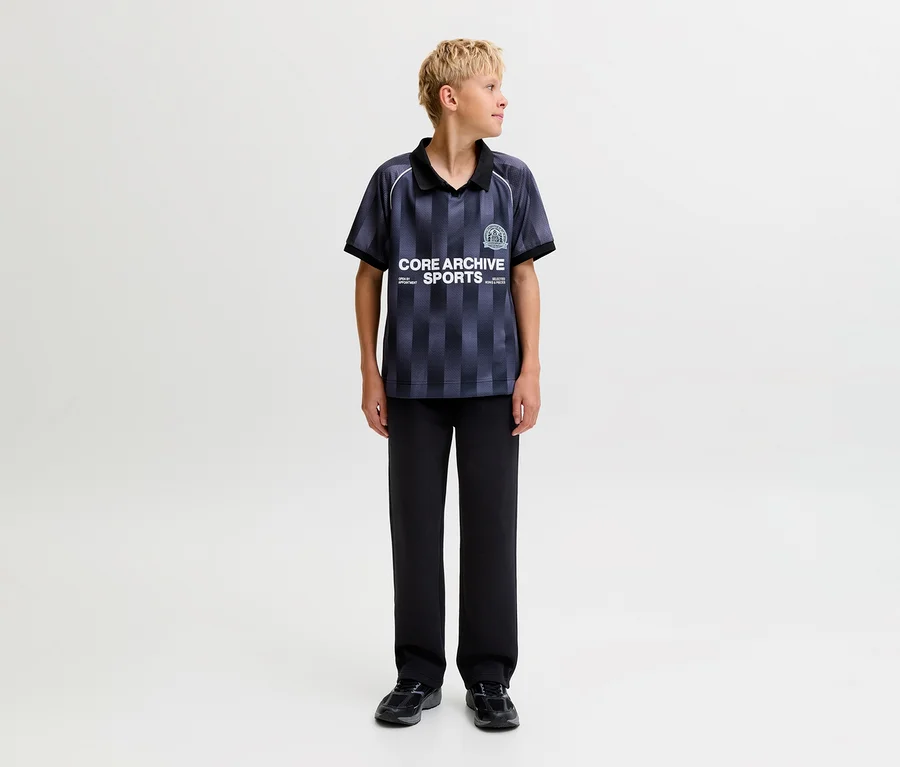 Junger Junge trägt ein dunkles gestreiftes Poloshirt und schwarze Jack&Jones Bradley Sweatpants, steht und blickt nach rechts.