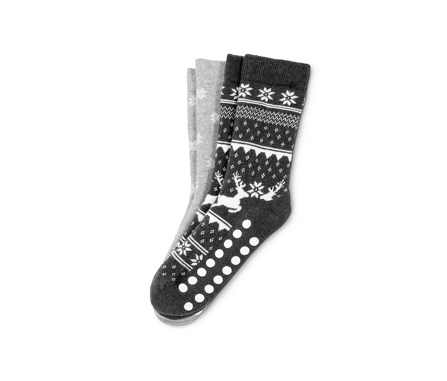 Zwei Paar Antirutsch-Socken. Ein Paar ist grau mit weißen Schneeflocken, das andere Paar ist dunkelgrau mit einem Muster aus Rentieren und Schneeflocken.