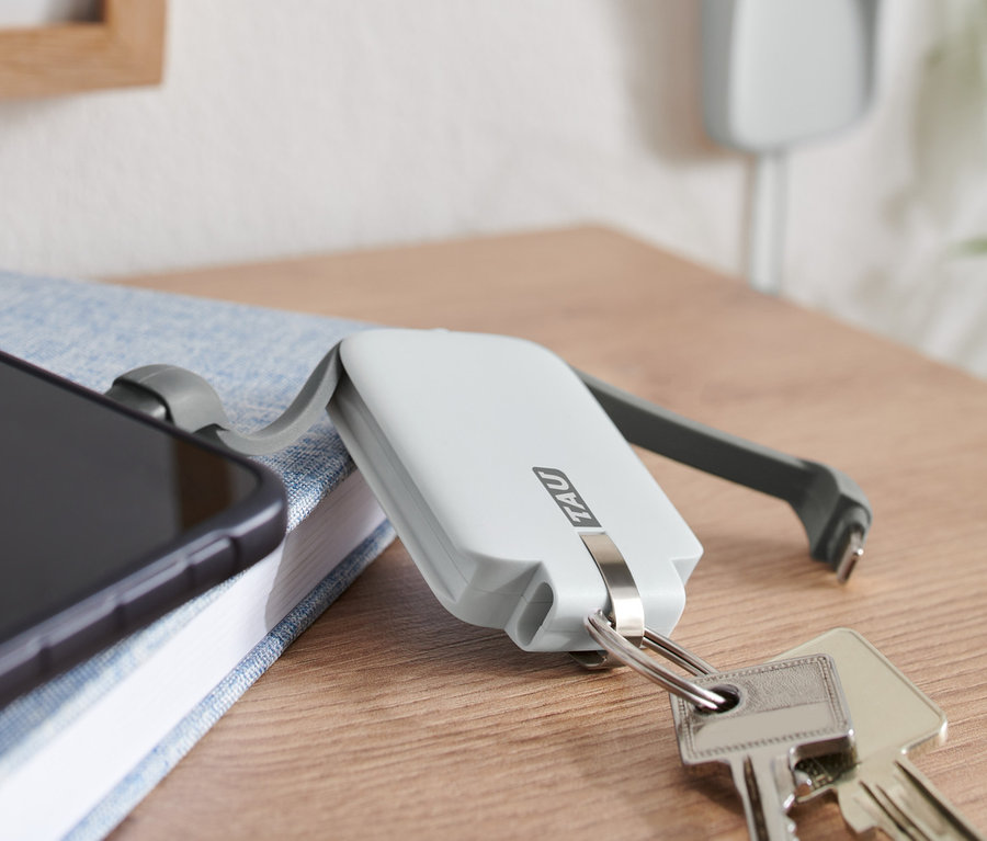 Handy liegt auf blauem Buch neben Schlüsseln und weisser TAU® 3-in-1-Keychain-Powerbank.