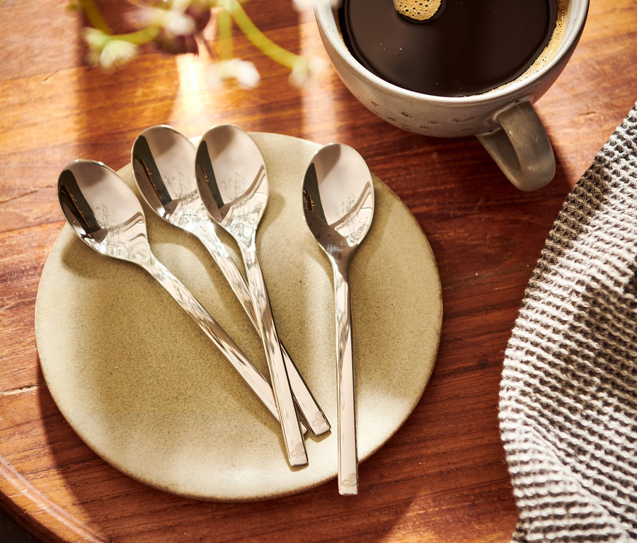 Vier Kaffeelöffel auf einem Teller neben einer Tasse Kaffee.