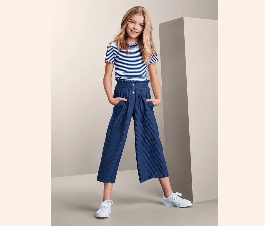 Mädchen posiert in plissierter Culotte und gestreiftem T-Shirt.