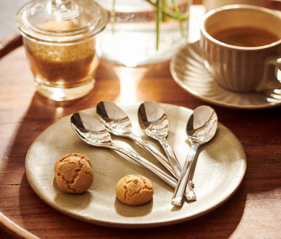 Auf einem Holztablett liegen 4 Espressolöffel neben zwei Keksen auf einem Teller.