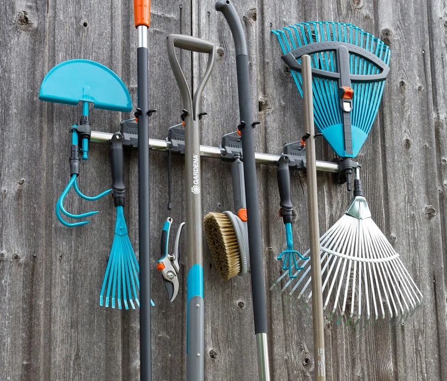 Gartengeräte wie Rechen, Schaufel und Bürste hängen an einem GARDENA »Gerätehalter« an einer Holzwand.