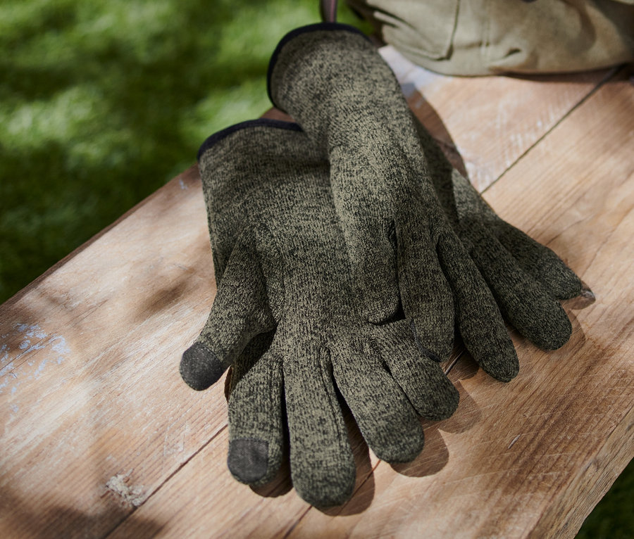 Ein Paar Strickfleece-Handschuhe liegen auf einer Holzbank neben einem Canvas-Rucksack.