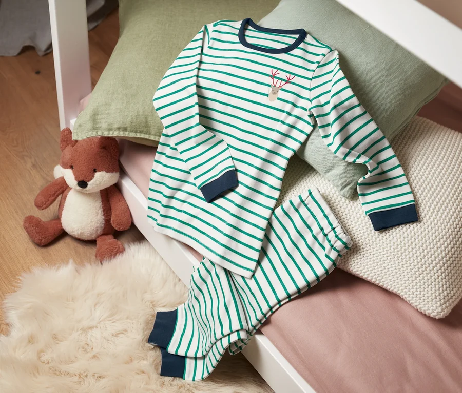 Ein gestreifter Interlock-Pyjama aus Bio-Baumwolle liegt auf einem Bett neben einem Fuchs Stofftier.