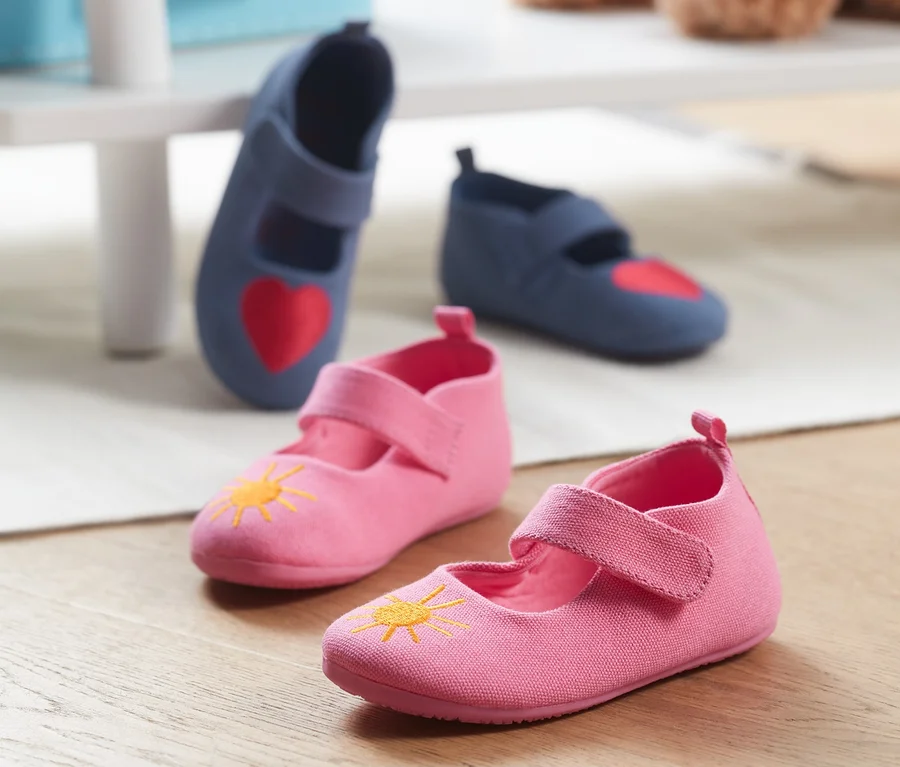 Zwei Paar Hausschuhe aus recyceltem Material: ein Paar rosa mit gelber Sonne, ein Paar blau mit rotem Herzen.