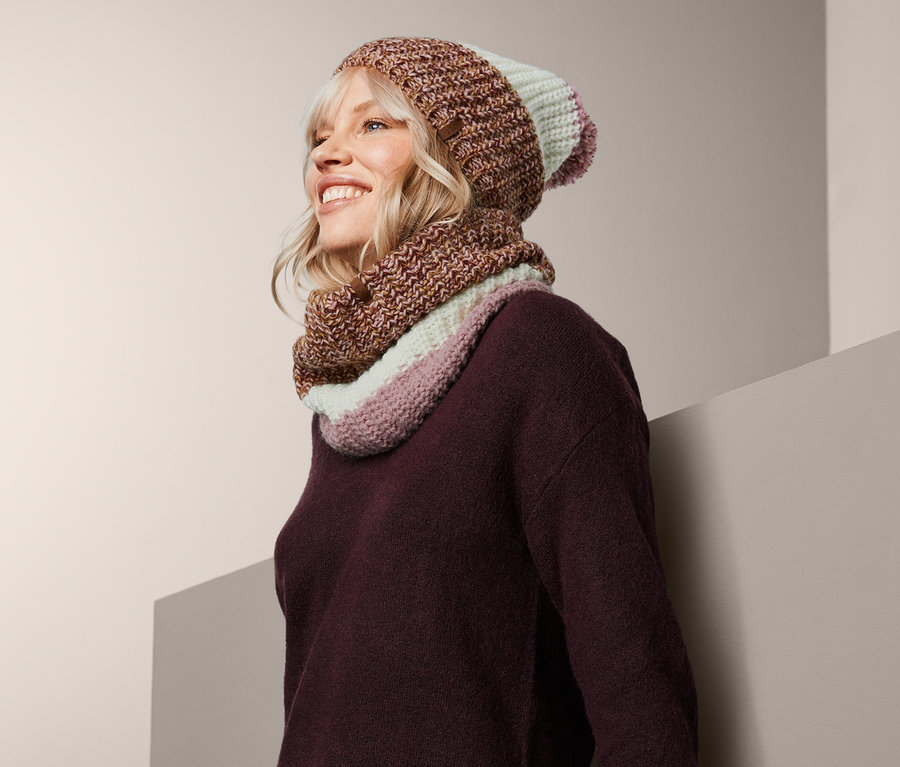 Frau mit blonden Haaren trägt einen Strickschlauchschal und eine Mütze.