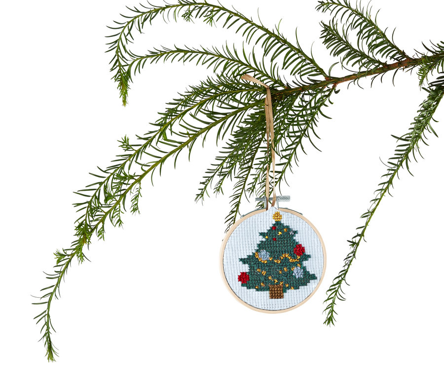 Grüner Nadelbaumzweig mit rundem Stick-Set, das ein Weihnachtsmotiv zeigt.