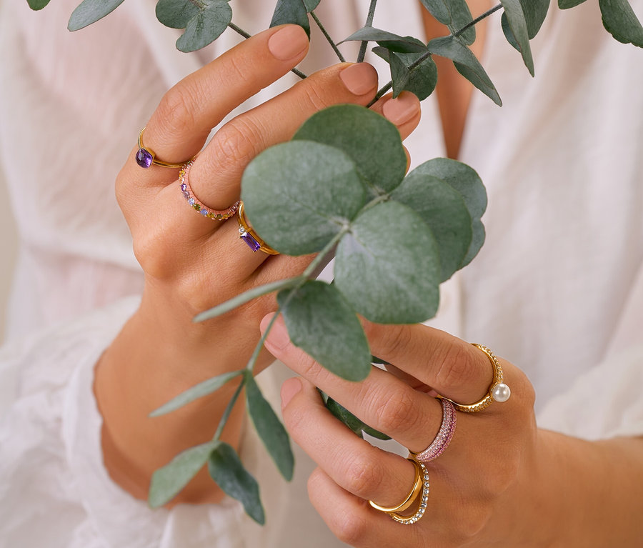 Frau hält Eukalyptuszweige und trägt 925 Silber Ringe, Multicolor Ring, 375 und 585 Gold Ring Amethyst, Doppel-Welle mit Kristallen Ring und pavé Ring.