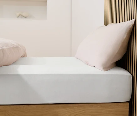 Bett mit weißem Jersey-Spannbettlaken und rosa Kissen.