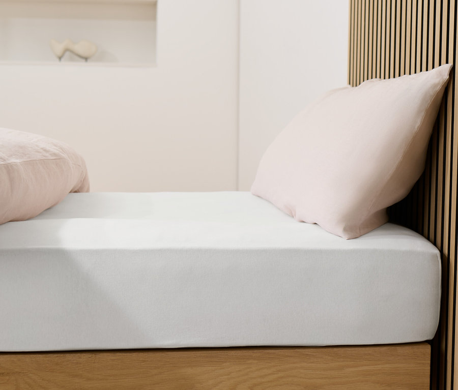 Bett mit weißem Jersey-Spannbettlaken und rosa Kissen.