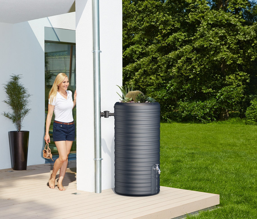 Frau kommt aus dem Haus neben dem graphitgrauen Garantia 2-in-1-Regentonne-Komplett-Set »Nordic«, ca. 300 l.