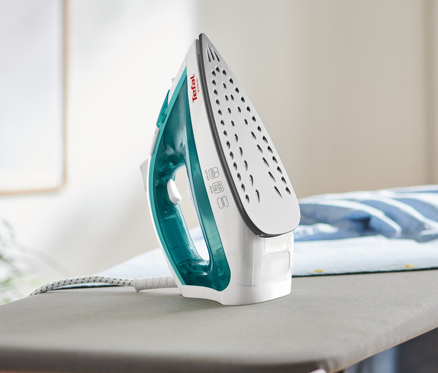 Ein Tefal-Dampfbügeleisen »Virtuo« steht auf einem Bügelbrett neben einem gefalteten, hellblauen Hemd.