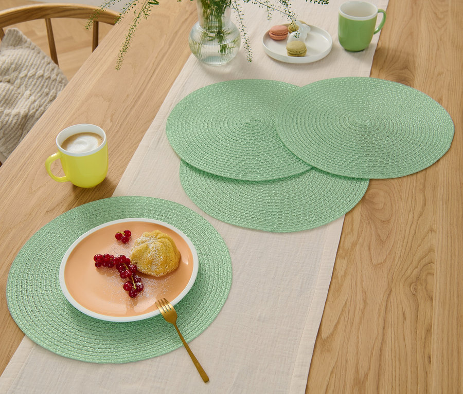 Vier grüne Platzsets auf einem Holztisch mit Tischläufer, auf einem Teller ein Dessert.