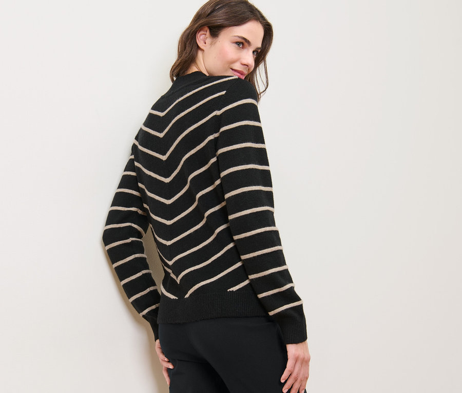 Frau blickt über die Schulter und trägt einen gestreiften schwarzen Strickpullover mit Stehkragen.