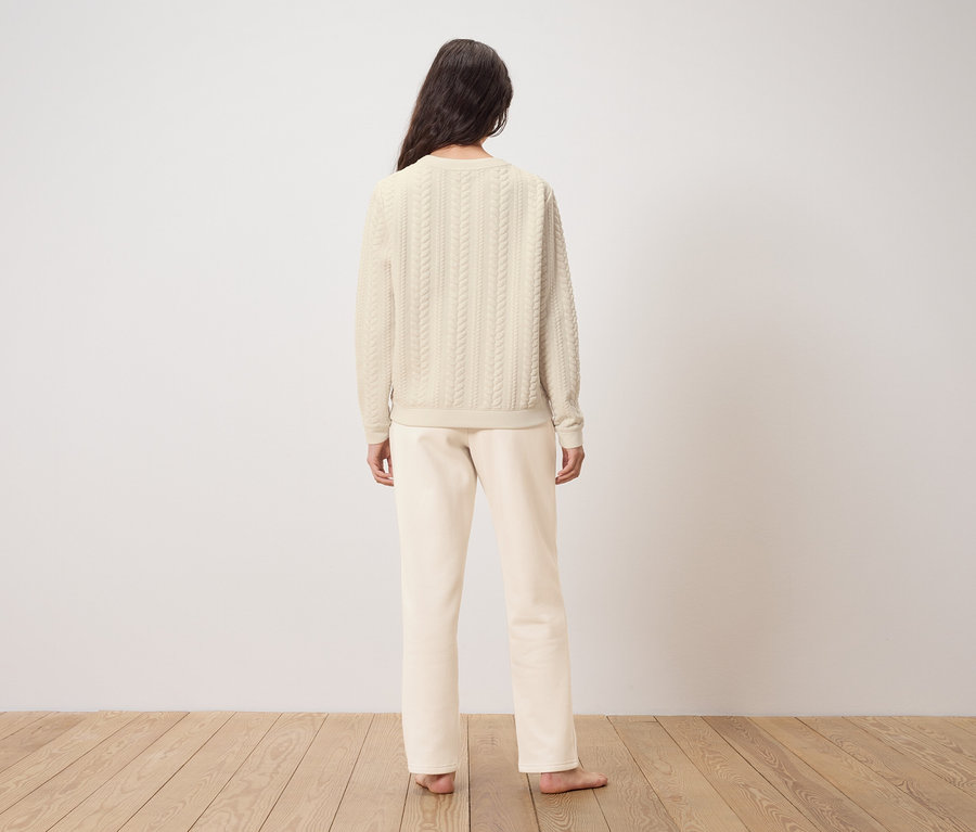 Frau steht mit dem Rücken zur Kamera und trägt einen cremefarbenen Pullover und eine Hose.