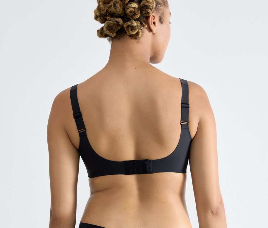 Rückansicht einer Frau mit Afro-Frisur, die einen schwarzen sloggi ZERO Feel 2.0 Soft BH trägt.