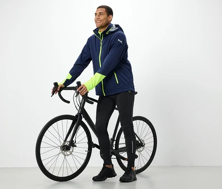 Mann in Jacke hält ein schwarzes Fahrrad.