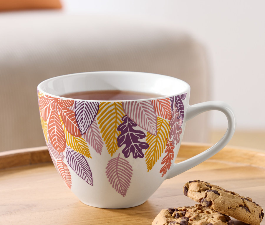 Eine Tasse Tee mit herbstlichem Blättermotiv und zwei Schokoladenkekse auf einem Holztablett.