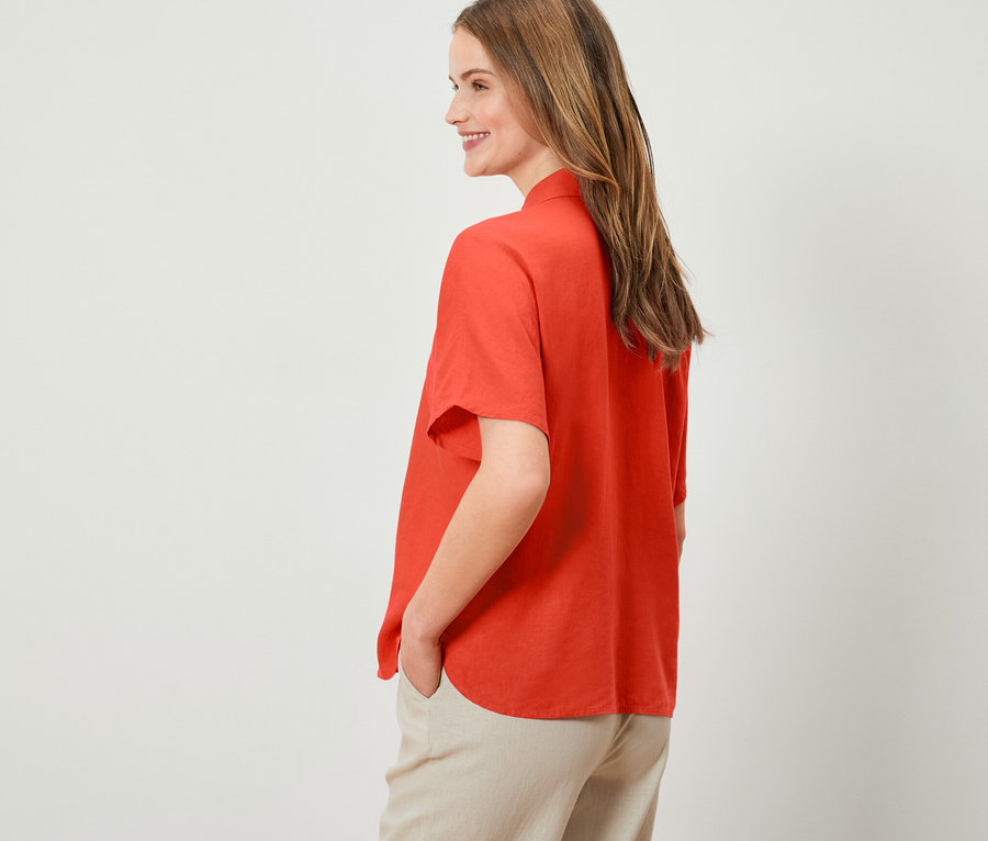 Frau posiert in orangefarbener Leinenbluse.