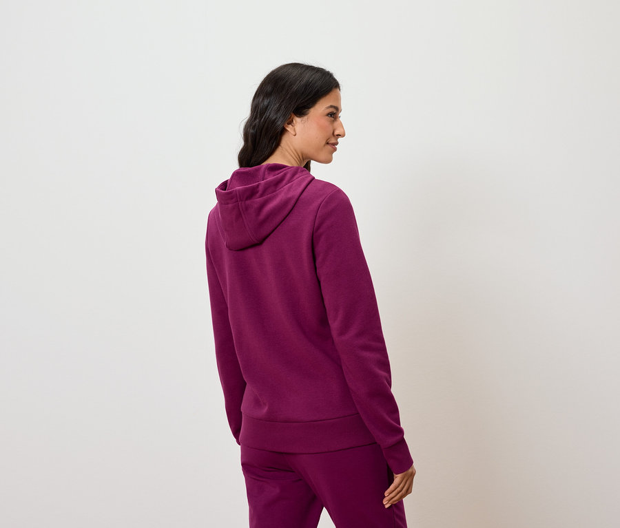 Frau posiert in einem violetten Kapuzenpullover und einer Hose.