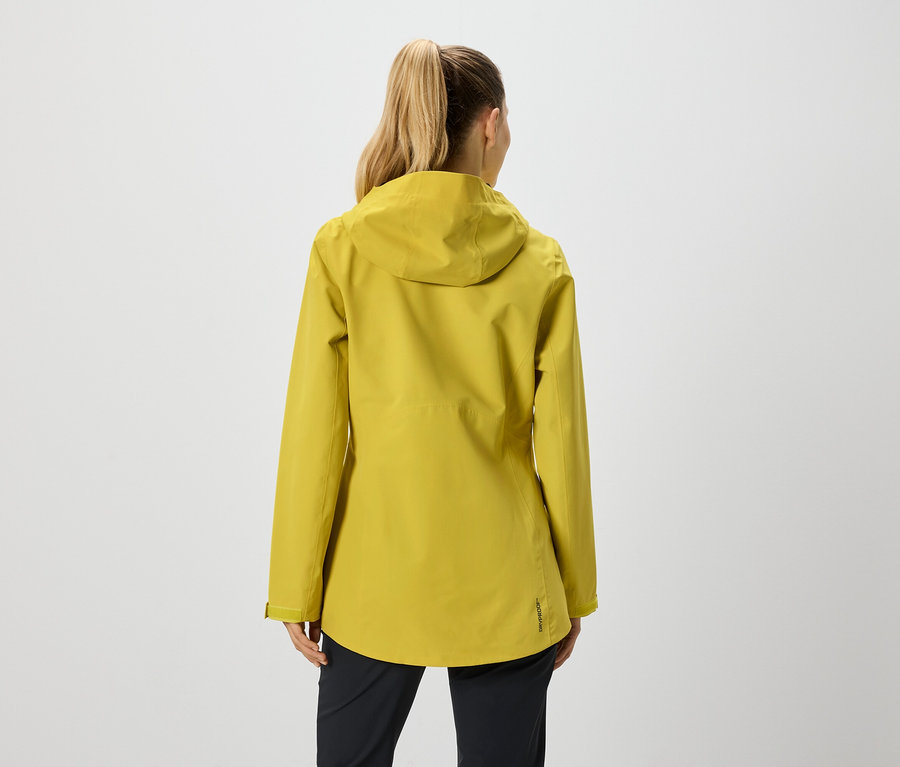 Rückansicht einer Frau mit Pferdeschwanz, die eine senfgelbe Jacke mit Kapuze und eine schwarze Hose trägt.