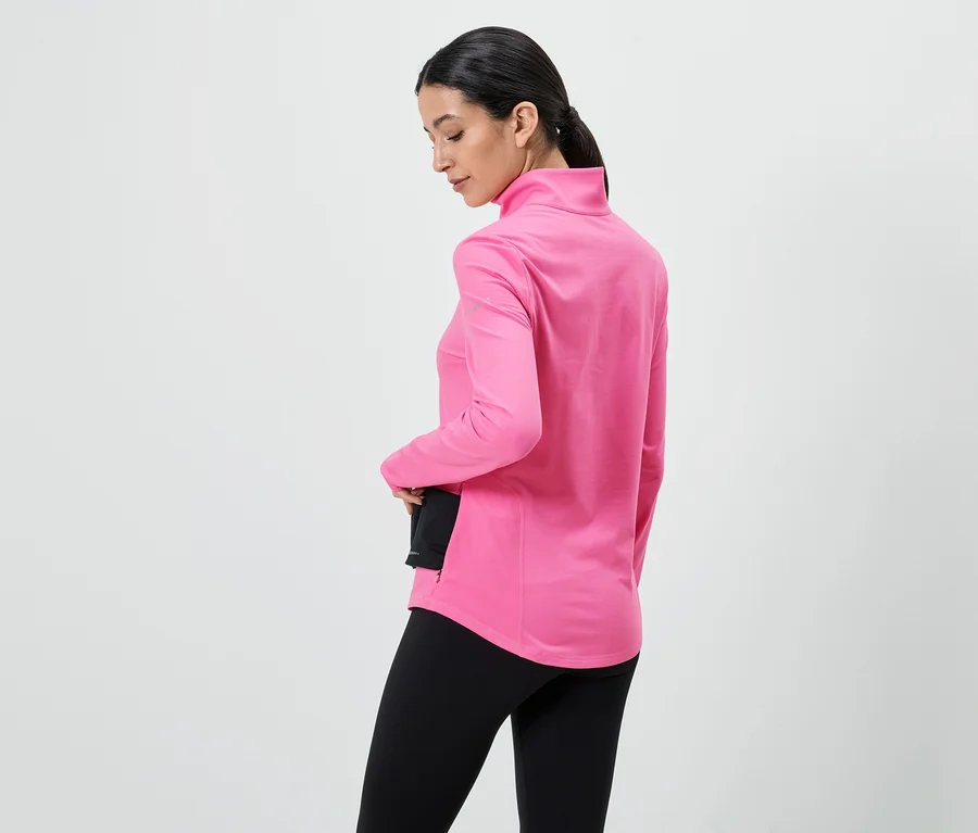 Frau von hinten, trägt pinkes Langarmshirt mit Stehkragen und schwarze Leggings, Hand in Tasche.