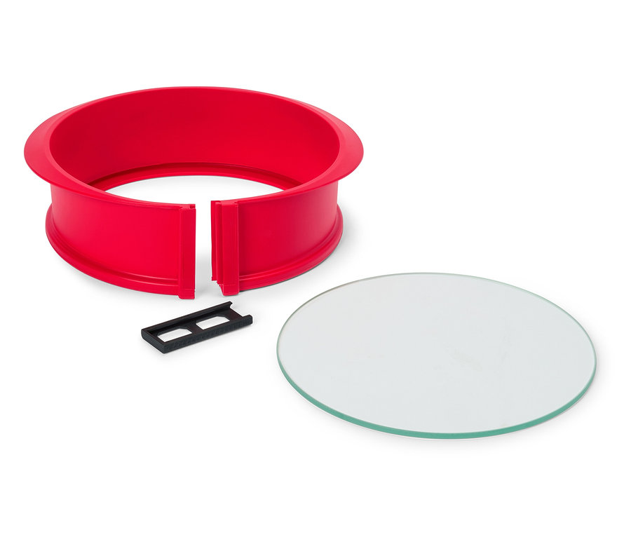 Roter, runder Kuchenrahmen mit schwarzem Clip und runder Glasplatte auf einem weißen Hintergrund.