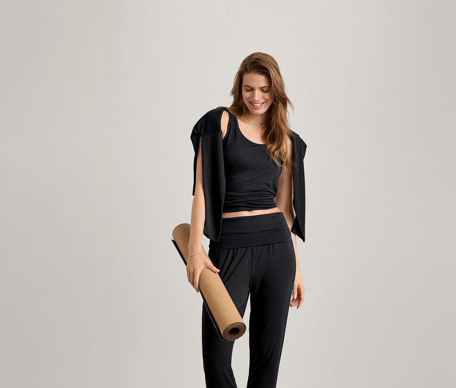 Frau hält eine Yogamatte und trägt ein schwarzes Da. 2-in-1-Sportshirt.