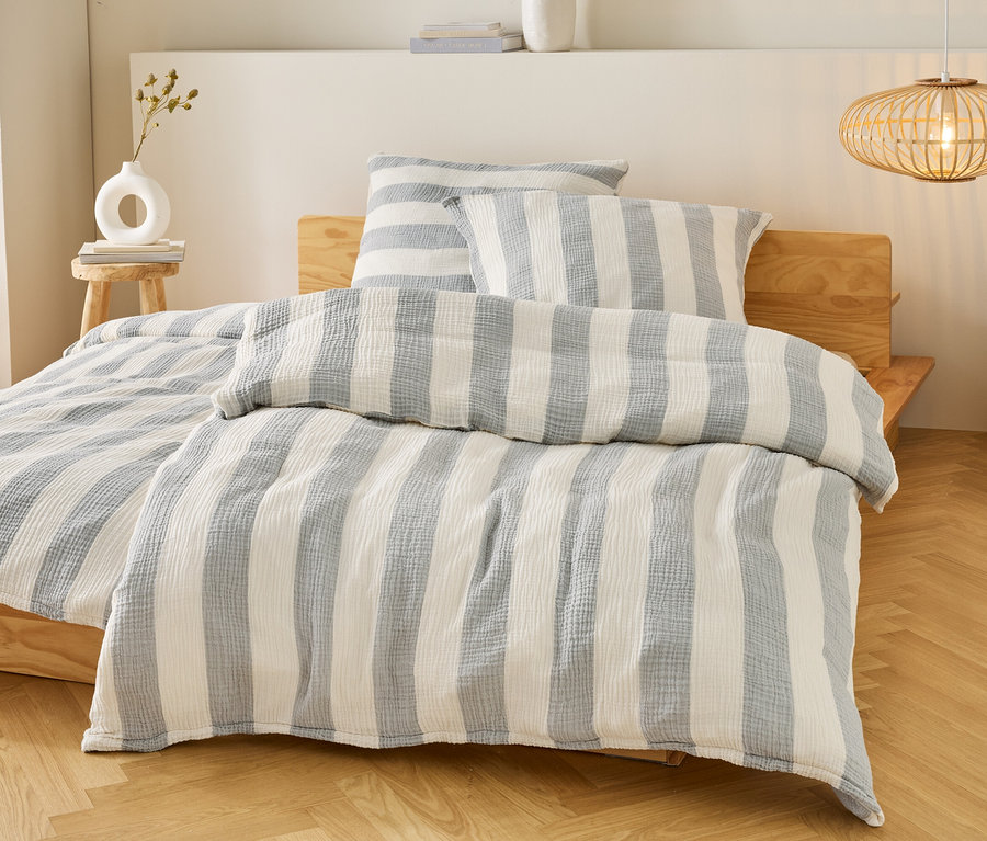 Bett mit blau-weiß gestreifter Bettwäsche und Kissen auf einem Holzbettgestell. Eine Lampe hängt über dem Bett.