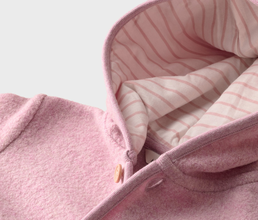 Nahaufnahme einer rosa Wolljacke mit Kapuze, die mit einem gestreiften Stoff gefüttert ist. Die Jacke ist mit einem hellbraunen Knopf geschlossen.