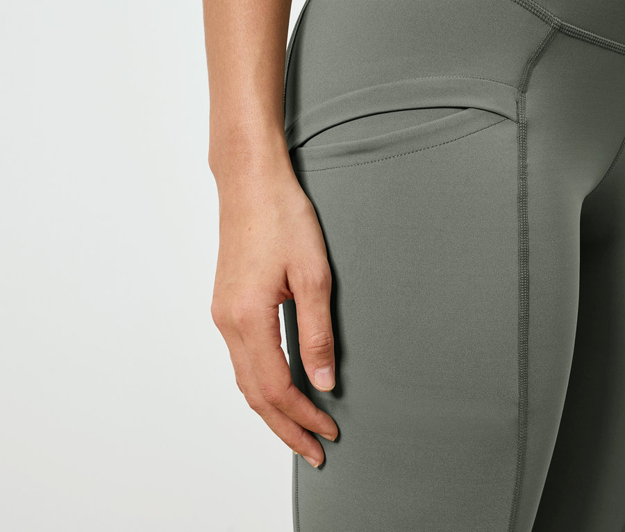 Nahaufnahme einer Person, die olivgrüne Leggings mit Seitentasche trägt.