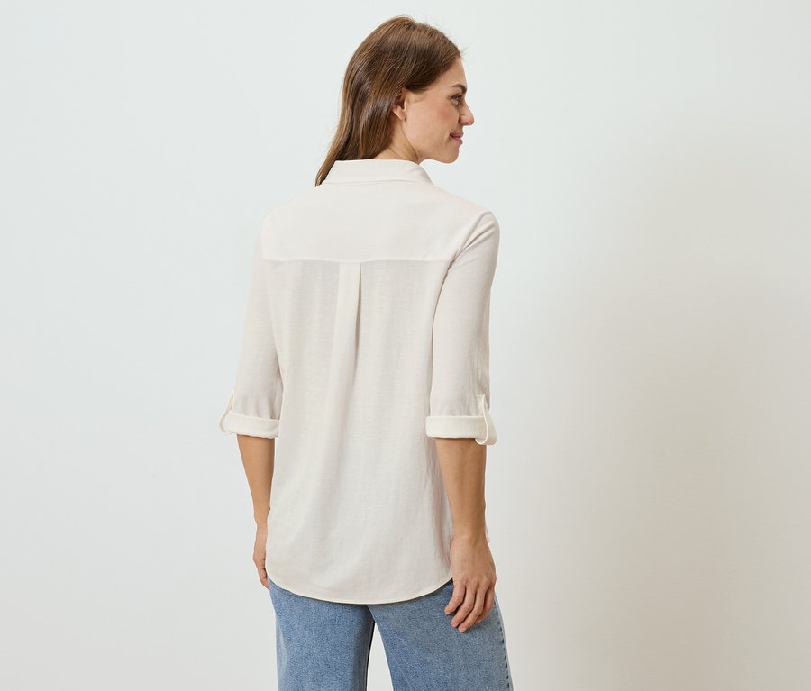 Rückansicht einer Frau mit langen braunen Haaren, die ein helles Hemd und Jeans trägt.