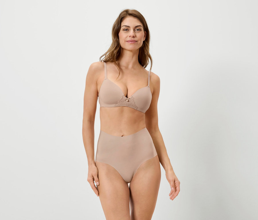 Frau trägt einen hautfarbenen BH und Slip vor einem weißen Hintergrund.