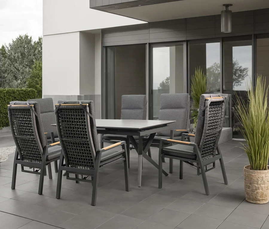 Sechs graue Stühle mit Armlehnen stehen um einen grauen Tisch auf einer Terrasse.