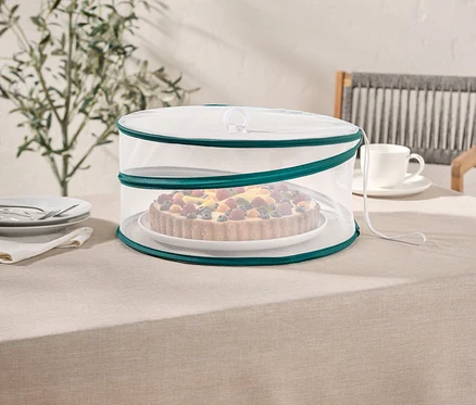 Obstkuchen unter einer weißen Netzabdeckung mit grünem Rand auf einem Tisch.