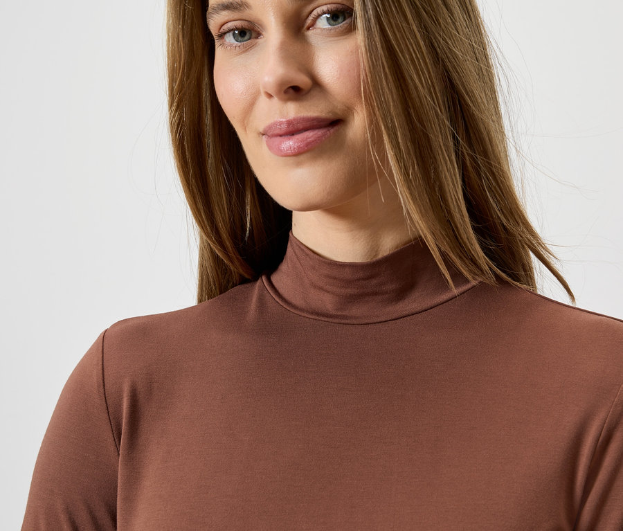 Porträt einer Frau mit langen braunen Haaren, die ein braunes Rollkragenshirt trägt.