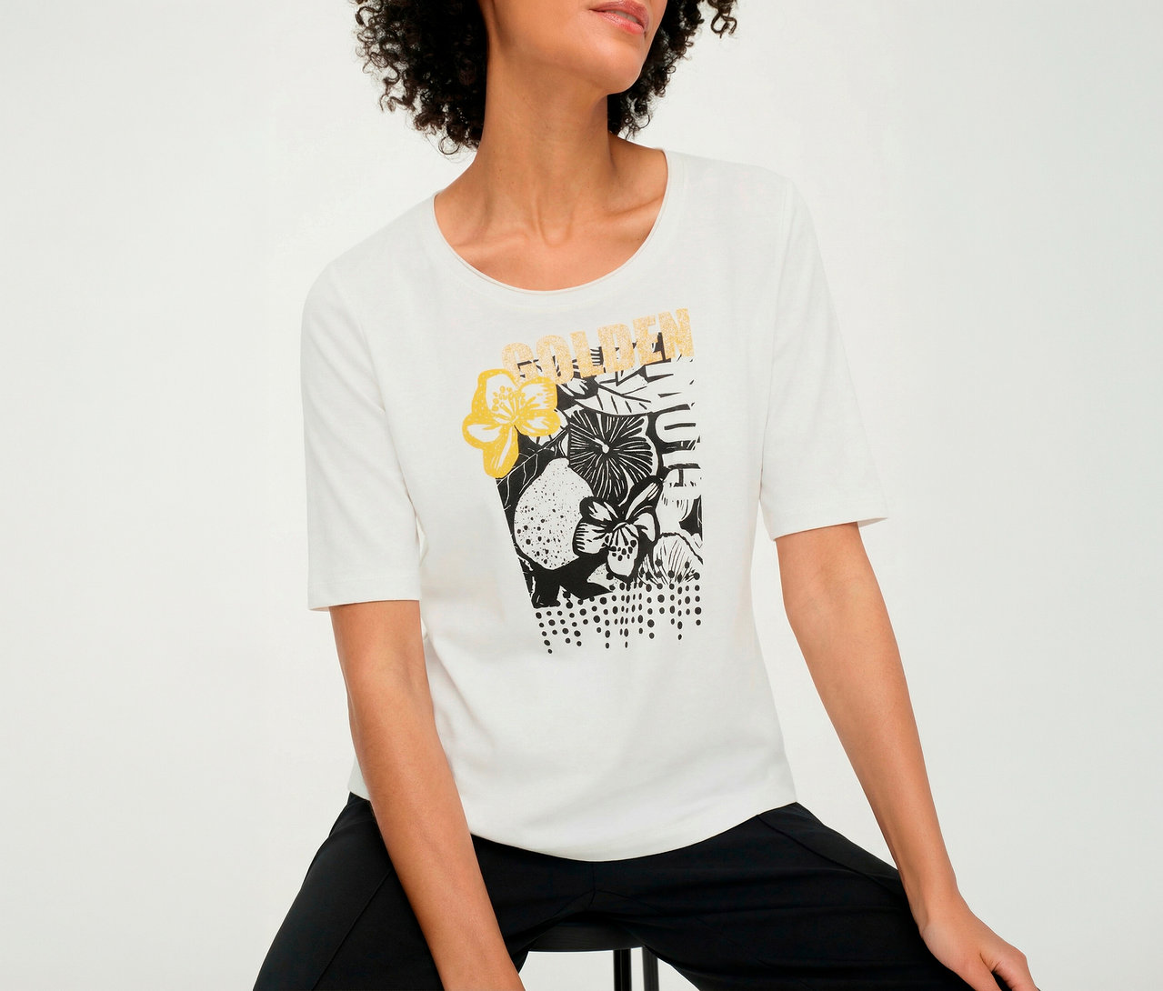 Frau mit weißem Olsen 3/4-Shirt mit Blumenmuster.