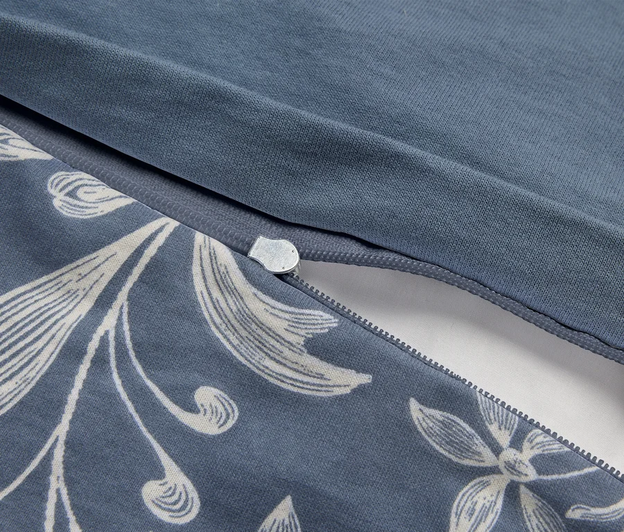 Nahaufnahme eines blauen Stoffes mit weißem Blumenmuster, der einen teilweise geöffneten Reißverschluss zeigt, unter dem weißer Stoff sichtbar ist.