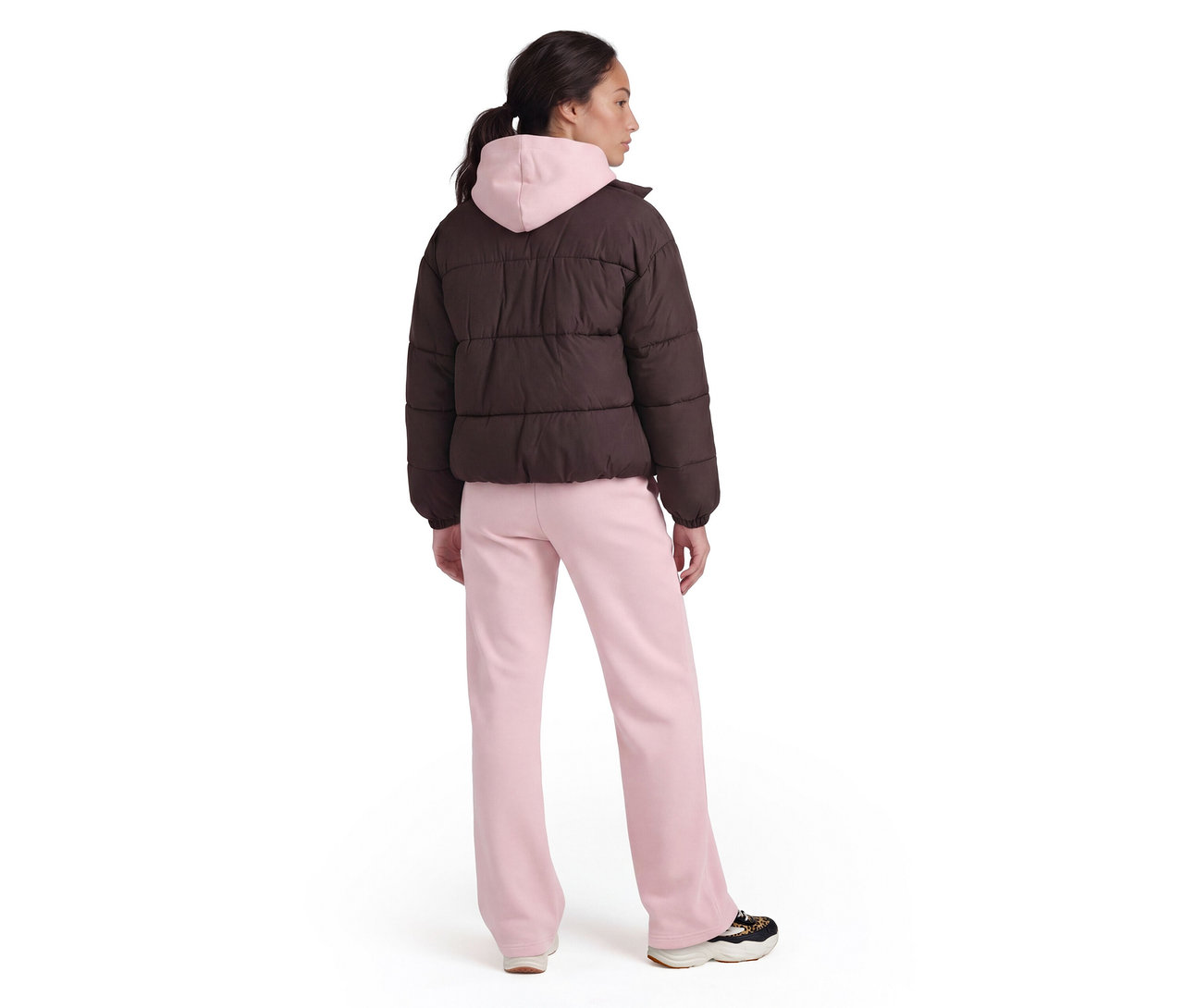 Person von hinten in brauner Steppjacke über rosa Hoodie, rosa Jogginghose und Turnschuhen.