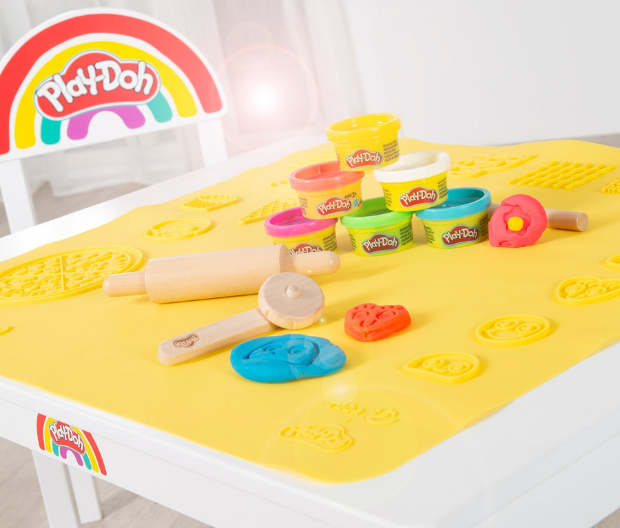 Auf einem roba x Play-Doh Sitzgruppen-Set liegen Play-Doh Dosen, gelbe Matte mit Formen, Nudelholz und Teigstücke.